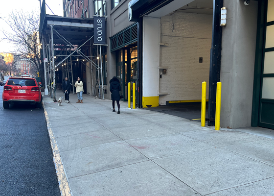 Image showing a sidewalk with people crossing a driveway leading into a building.