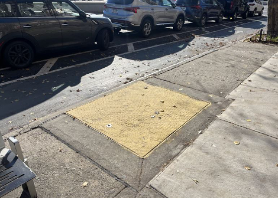 Image of an emergency exit hatch (painted yellow) located in the sidewalk adjacent to the curb.