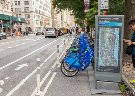 Image of a citi bike station located in the roadway in between a bike lane and the curb.