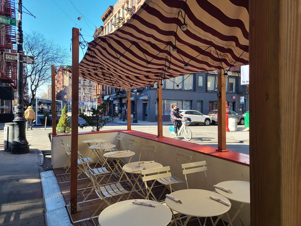 tables and chairs are ready for patrons inside a corner roadway cafe on a sunny day