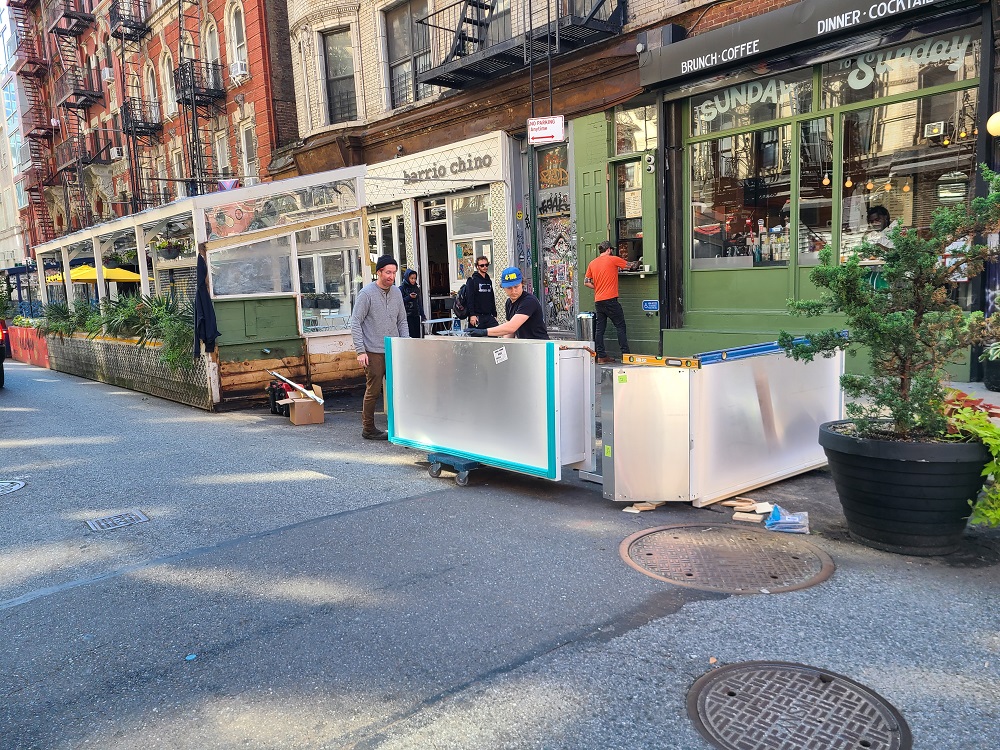 A team assembles the barriers for a corner roadway cafe