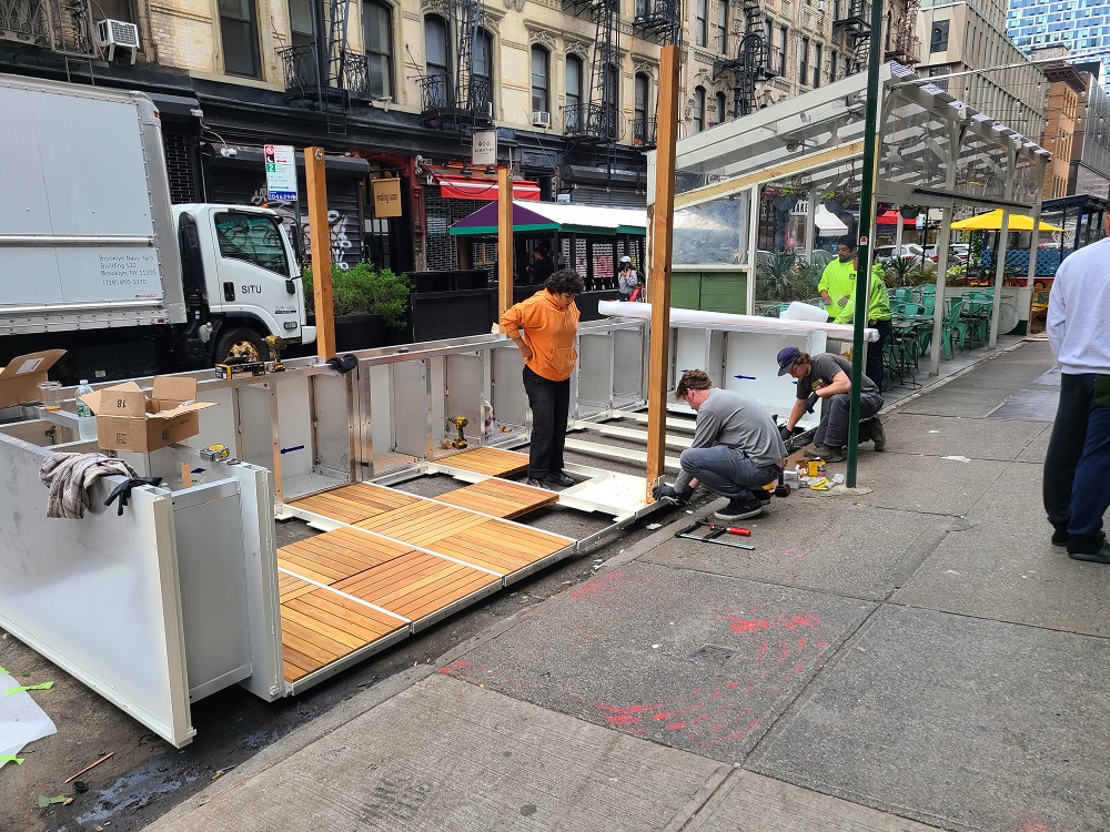 A team assembles the flooring base and panels at a corner roadway cafe
