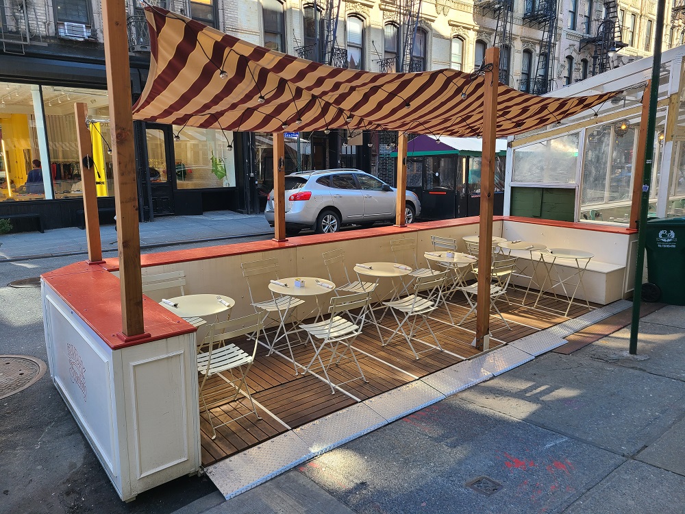 Corner setup roadway cafe with tables and chairs and an awning overhead